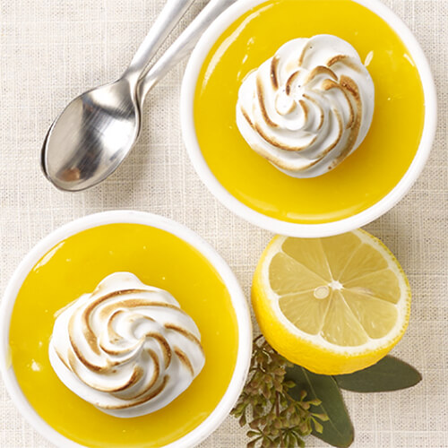 Delicious lemon meringue shooters filled with a sweet meringue, a tart lemon curd, and a savory crust, served in ramekins atop a linen tablecloth.