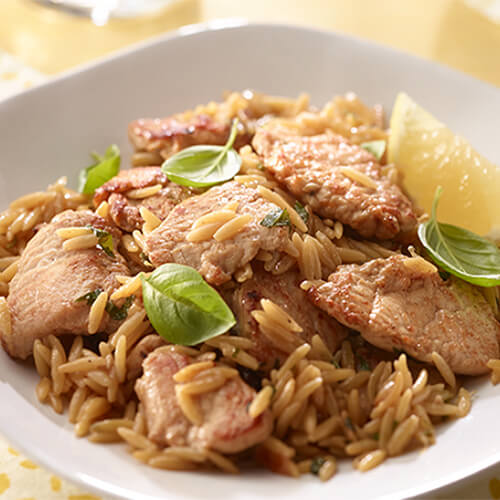 A hearty portion of orzo, parmesan, lemon, and lean turkey served in a white bowl on a yellow patterned cloth.