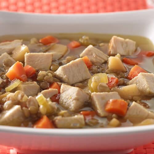 A savory, delicious, portion of turkey, simmered with herbs, garlic, and rutabaga, served in a white bowl on a red woven table mat.