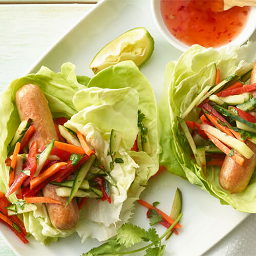 Two turkey franks on a lettuce wrap topped with vegetables on a white plate.