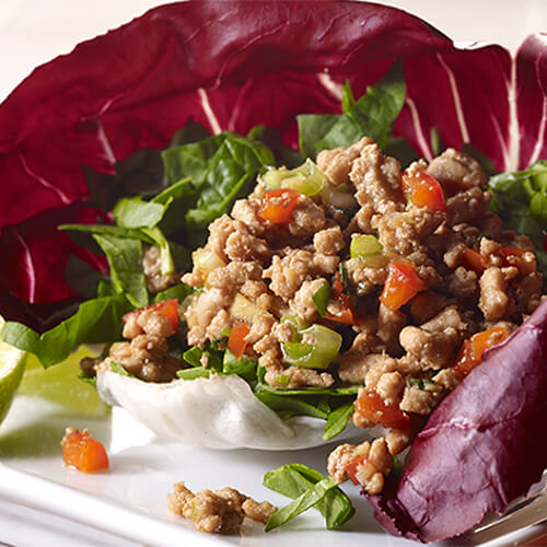 Turkey tacos chock full of vegetables and turkey served in radicchio lettuce cups on a white plate.