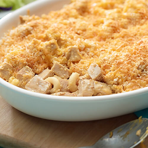 A creamy breaded pasta bake filled with macaroni, cheese, and turkey, served in a white tray on a wooden block.