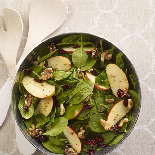 Apple cranberry walnut salad in a grey bowl on a beige patterned tablecloth.