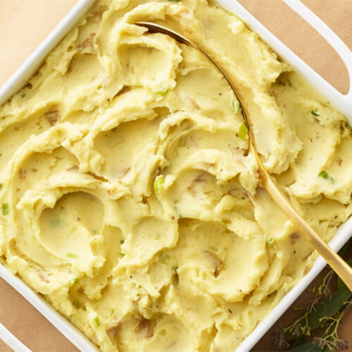 Goat cheese mashed potatoes in a white dish with a metal spoon.