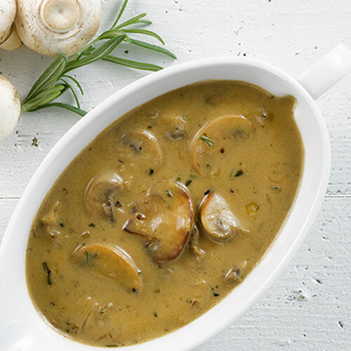 Mushroom gravy in a white tureen on a white table with a sprig of rosemary.
