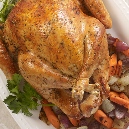 Slow roasted whole turkey with vegetables on a white plate garnished with a sprig of cilantro.