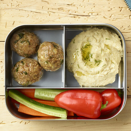 Herbed Mediterranean-style turkey meatballs, served with a side of vegetables and mashed potatoes in a metal divided tray, on a wooden table.