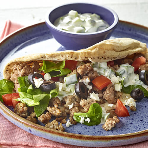 A pita chock full of veggies ground turkey and tzatziki sauce on a blue plate, on a coral napkin on a wooden table.