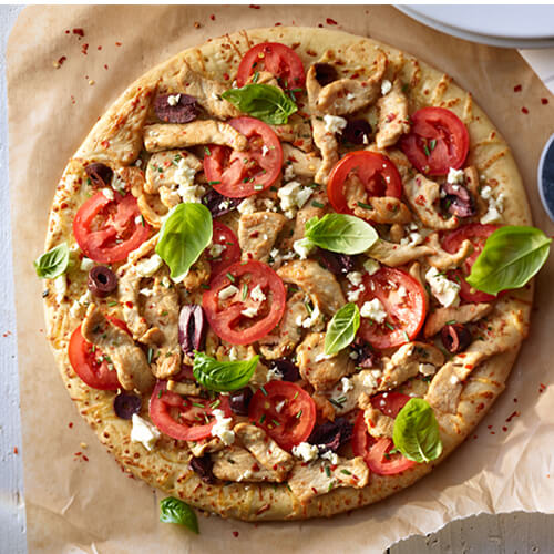 Mediterranean turkey pizza garnished with greens on a wood pizza pan.