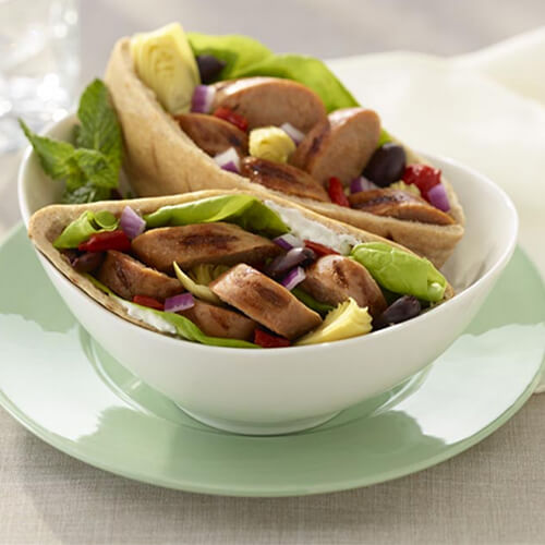 Pita pockets filled with turkey sausages and a hearty portion of veggies and tzatziki served on a white bowl atop a mint green plate.