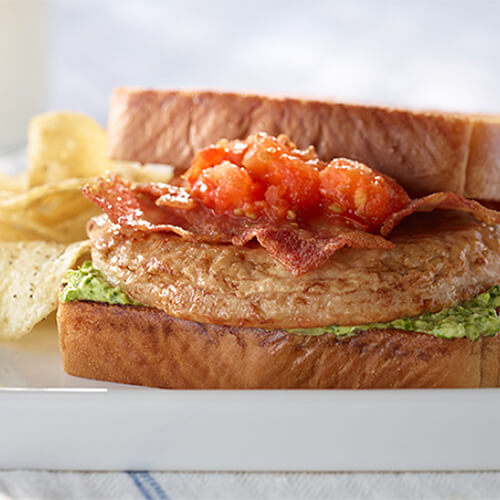 A hearty turkey club made with sautéed tomatoes, parmesan cheese, and a lettuce mayo, served on a white plate with potato chips.