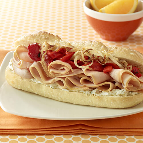 A savory containing an herb spread, Mesquite smoked turkey, bell peppers, and sautéed onions, on a white plate atop an orange cloth.