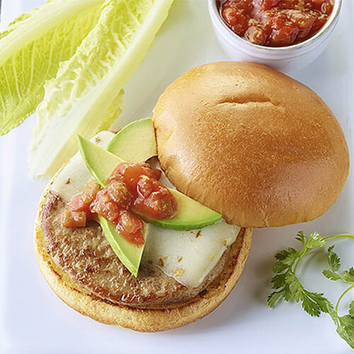 Turkey burger topped with cheese, avocado slices, and salsa on a white background next to leaves of Romaine lettuce.