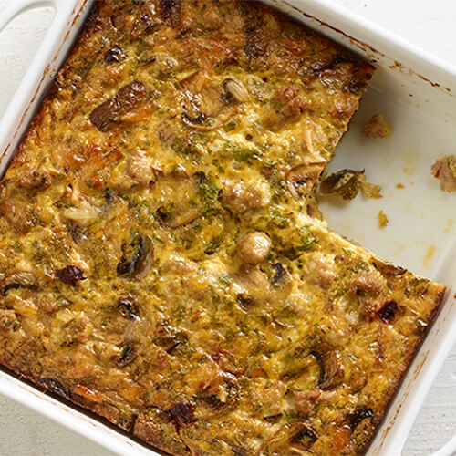 A flavorful egg and turkey frittata made with green pepper, mushrooms, and chipotle peppers, served in a white baking dish on a wooden table.