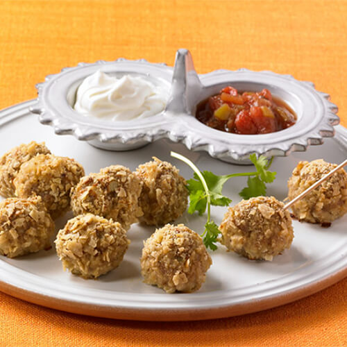 Bite-sized, coated, turkey meatballs, garnished with cilantro, served with a side of sour cream and salsa, served on a white plate.