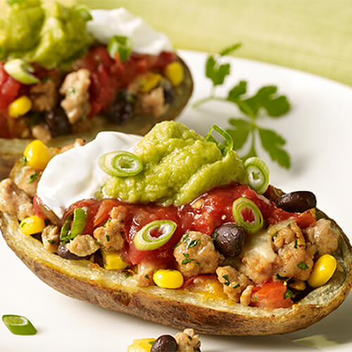 Potato skins stuffed with guacamole, sour cream, salsa, ground turkey, veggies and melted cheese, served on a white plate.