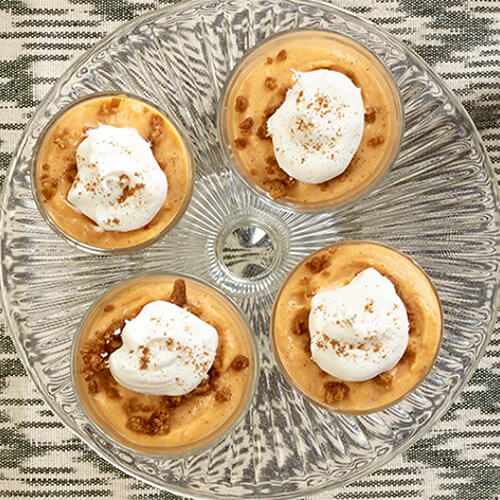 Miniature dessert shooters made with spiced pumpkin and cheesecake filling, served on a glass tray.