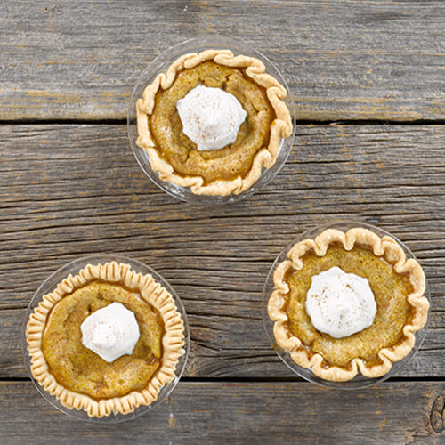 Mini pumpkin pies with a dollop of whipped cream on a wood table.