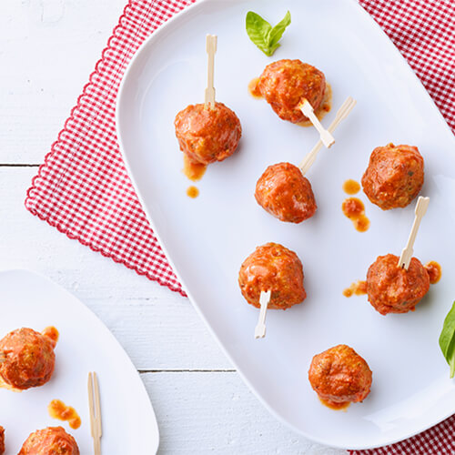 Miniature turkey breaded meatballs, dipped in marinara sauce, served in a white tray on a red checkered cloth.