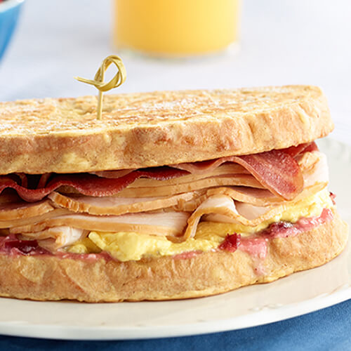 A traditional Monte Cristo sandwich made with battered bread, cranberry cream cheese spread, bacon, eggs, and turkey.