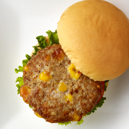 A burger patty made with turkey and cheese curds, topped with lettuce, tomato and onion, served with a container of ketchup and a cup containing sweet potato fries, served on a white tray.