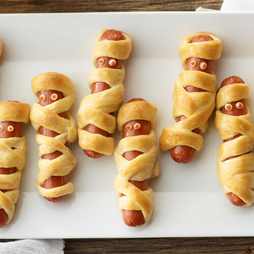 Halloween inspired mummy shaped turkey franks with crescent rolls on a white background.