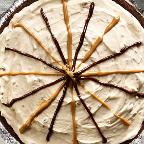 A chocolate graham cracker cheese cake, filled with peanut butter spread, cream cheese and honey, served in a pie tin on a light gray table.