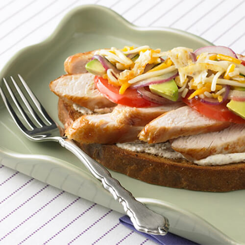 An open-faced sandwich topped with sweet Italian turkey sausage, fresh basil, marinara and melted cheese, served with a side salad in a gray bowl atop a wooden table.