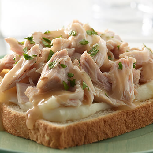 An open face turkey sandwich topped with sautéed pepper strips, herbed cream cheese, and green onions, served on a white platter.