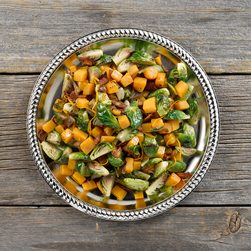 Orange glazed brussels sprouts and butternut squash in a grey bowl on a wood table.