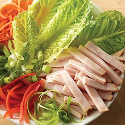 A white plate leafy Romaine lettuce, carrot strips, strips of JENNIE-O® Turkey Breast and red bell pepper slices.