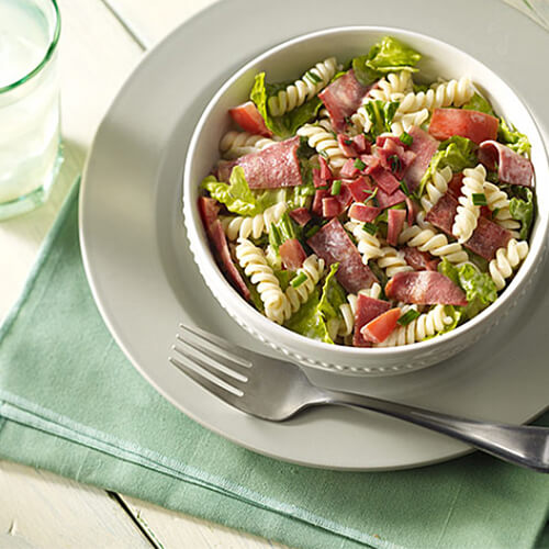 Fresh romaine lettuce, turkey bacon, thyme-simmered tomatoes filled with a creamy chive sauce on a white studded bowl and a silver plate.