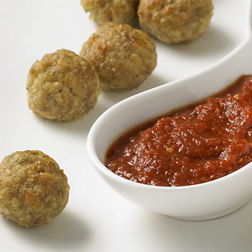 Meatballs made with basil pesto, Parmesan cheese and lean ground turkey served with a red pepper sauce in a white sauce tray with a white background.