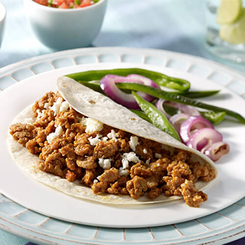 A hearty turkey taco made with grilled Poblano peppers, onions and fresh pico de gallo, served on a white plate with a side of fajitas atop a blue painted plate and cloth.