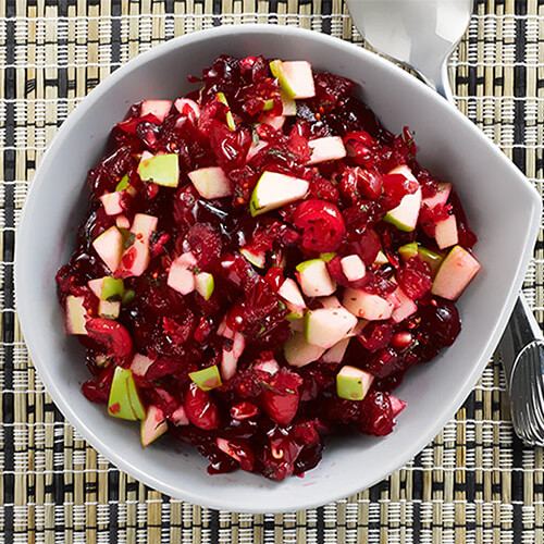 Pomegranate apple cranberry relish on a white bowl on a striped tablecloth.