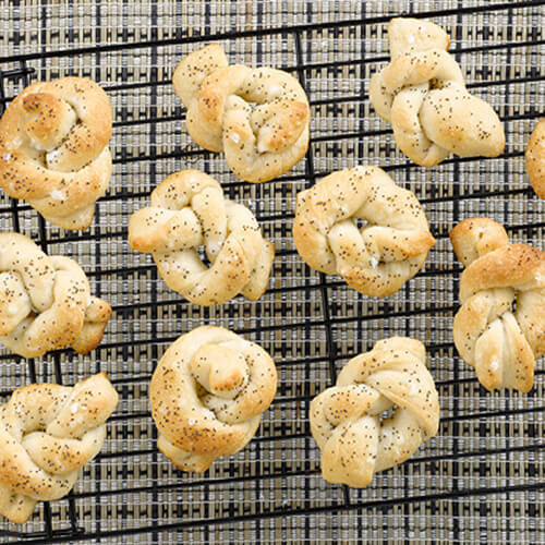 Poppyseed twisted mini rolls on a wire cooling rack.