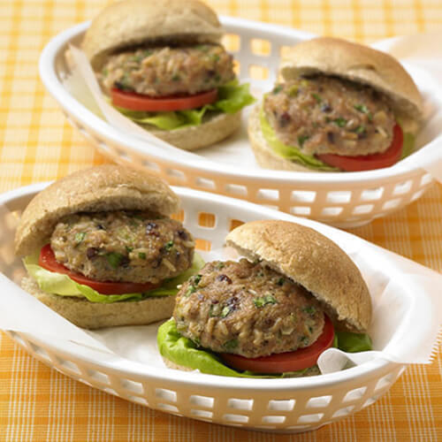 Sliders made with turkey, cranberries, and brown rice, with lettuce, tomatoes and onions served in a white serving basket on a yellow tablecloth.