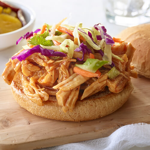 Pulled turkey breast tenderloin sandwiches, covered in barbecue sauce, topped with coleslaw, on a wooden tray.