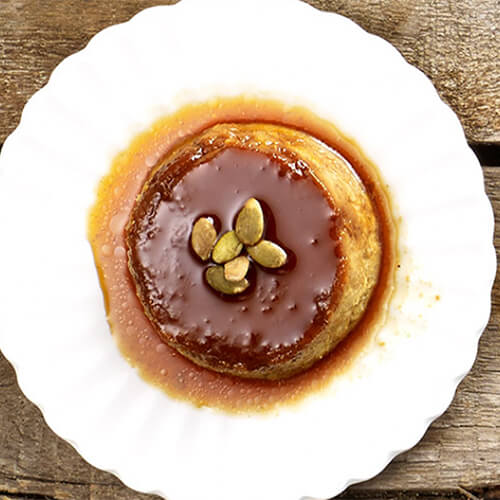 A rich and creamy pumpkin flan, served on a white plate atop a wooden table.