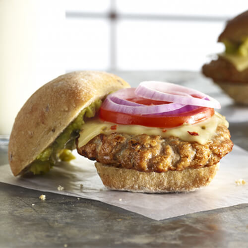 Turkey burger topped with pepper jack cheese, tomatoes, onions and lettuce on a white plate on a granite countertop.