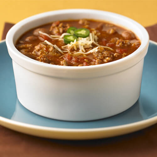 Turkey chili topped with cheese and onions in a white bowl on a blue plate.