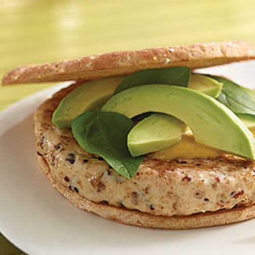 Turkey burgers are loaded with quinoa, red onion and goat cheese are topped with sliced avocado and served with a side of sweet potato fries, on a white plate atop a lime green tablecloth.