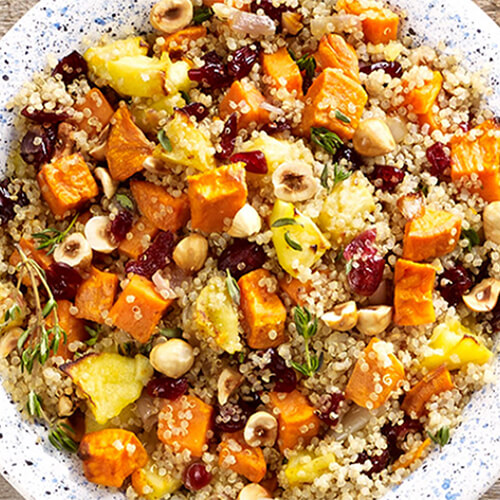 Potatoes and quinoa mixed with fall flavors such as sweet potatoes, apples & hazelnuts, served in a white plate atop a wooden table.