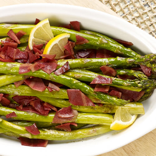 Crisp asparagus roasted with salty turkey bacon served in a white bowl on a linen cloth.