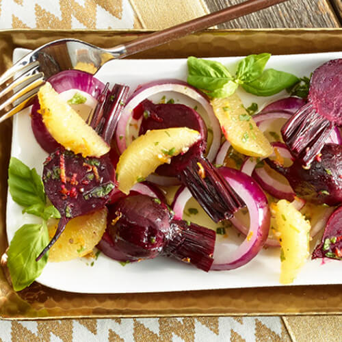 A delectable filled with orange slices, roasted beets and red onions, served on a white platter atop a golden tablecloth.