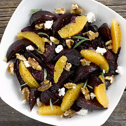 Roasted beets and orange with goat cheese and walnuts on a white bowl on a grey wood table.