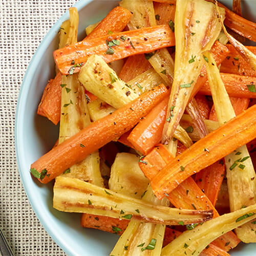 Seasoned and roasted carrots & parsnips, sprinkled with parsley in a blue bowl on a linen tablecloth.