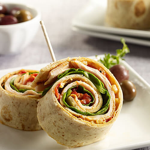 Roasted red pepper turkey pinwheels held together with toothpicks on a white plate.