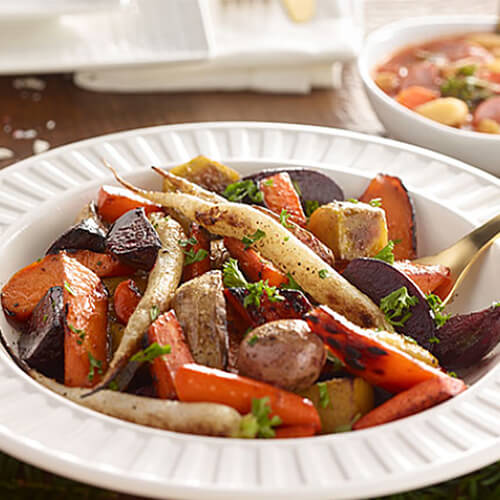 Carrots, potatoes, and other roasted root vegetables in a white bowl.