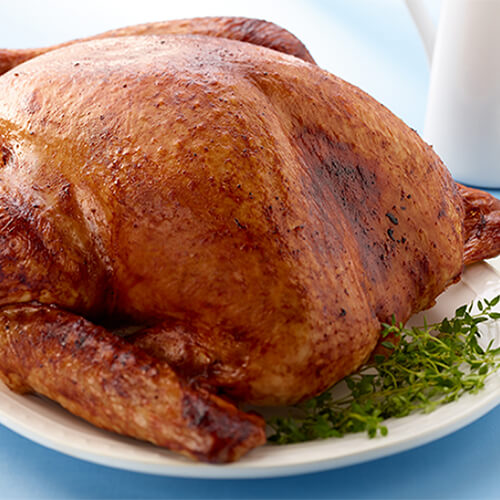 A whole turkey glazed served with herbs on a white plate with a side of cranberry chutney and gravy.